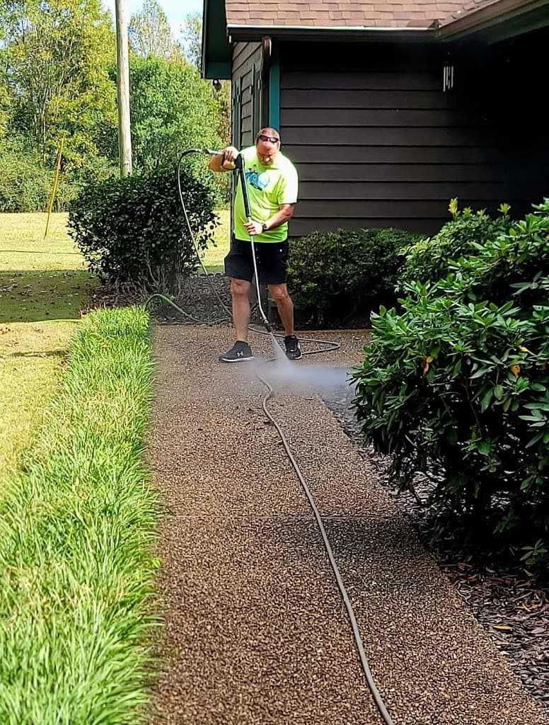Technician pressure washing a paver walkway between hedges